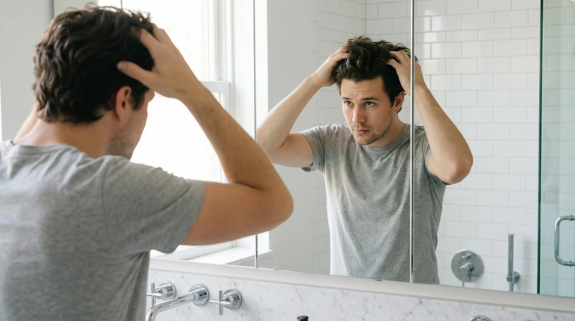 Man styling his hair at home in bathroom mirror, hands running through hair